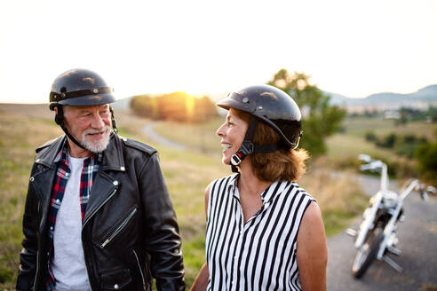 Ein Porträt eines fröhlichen älteren Paares, das mit dem Motorrad auf dem Land unterwegs ist und sich unterhält. - HPIF21815