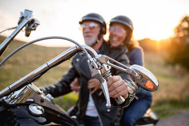 Ein fröhliches älteres Ehepaar reist mit dem Motorrad auf dem Lande bei Sonnenuntergang. - HPIF21828
