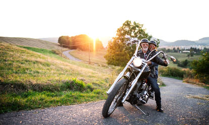 A cheerful senior couple travellers with motorbike in countryside. Copy space. - HPIF21829