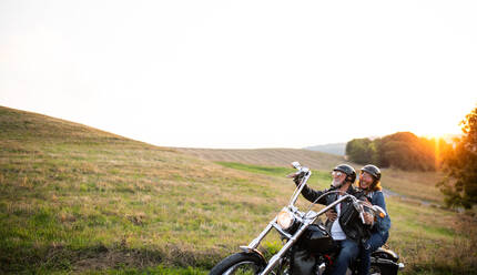 A cheerful senior couple travellers with motorbike in countryside. Copy space. - HPIF21832