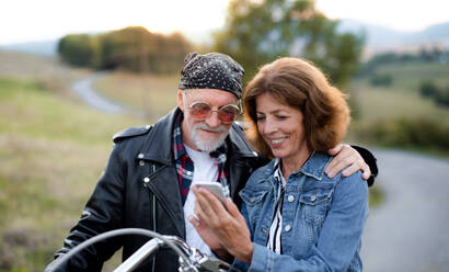 Ein fröhliches älteres Ehepaar reist mit dem Motorrad durch die Landschaft und benutzt ein Smartphone. - HPIF21839