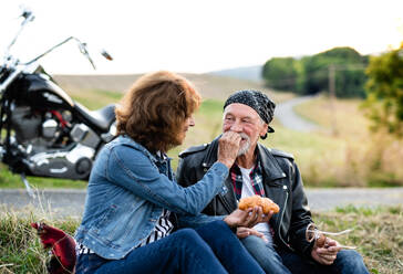 Ein Porträt eines fröhlichen älteren Paares, das mit dem Motorrad auf dem Land unterwegs ist und einen Snack zu sich nimmt. - HPIF21841