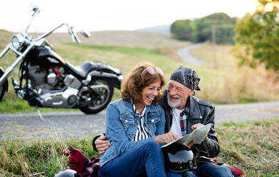 Ein fröhliches älteres Ehepaar reist mit Karte und Motorrad durch die Landschaft. - HPIF21846