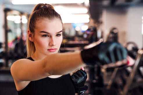 Vorderansicht eines jungen Mädchens oder einer Frau mit Handschuhen, die in einem Fitnessstudio trainieren. - HPIF21873