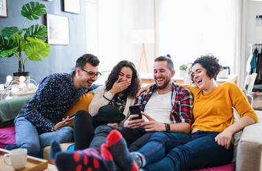 Eine Gruppe junger, fröhlicher Freunde mit Smartphone sitzt auf dem Sofa im Haus, Haus-Sharing-Konzept. - HPIF21902