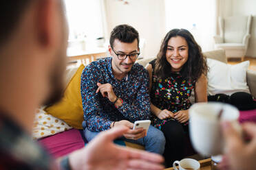 Eine Gruppe junger, fröhlicher Freunde mit Smartphone sitzt auf dem Sofa im Haus, Haus-Sharing-Konzept. - HPIF21904