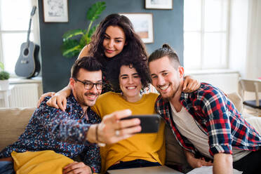 Freunde halten glückliche Momente bei der gemeinsamen Nutzung des Hauses fest und posieren mit ihrem Smartphone für ein Selfie auf dem Sofa - HPIF21923