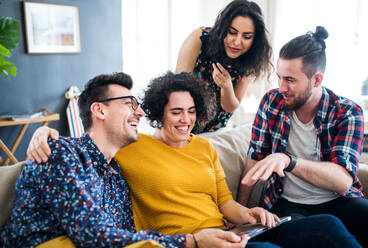 A group of young cheerful friends with tablet sitting indoors, house sharing concept. - HPIF21924