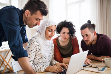 Eine multiethnische Gruppe junger, fröhlicher Freunde mit Laptop, die drinnen am Tisch sitzen, Konzept der Hausgemeinschaft. - HPIF21938