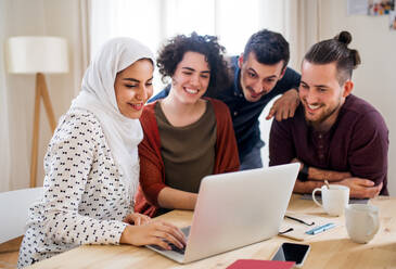 Eine multiethnische Gruppe junger, fröhlicher Freunde mit Laptop, die drinnen am Tisch sitzen, Konzept der Hausgemeinschaft. - HPIF21939