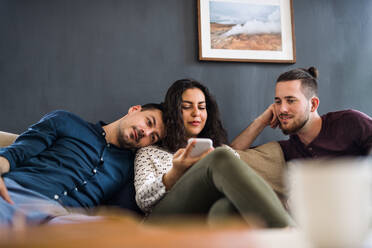 Eine Gruppe junger, fröhlicher Freunde mit Smartphone sitzt auf dem Sofa im Haus, Haus-Sharing-Konzept. - HPIF21946