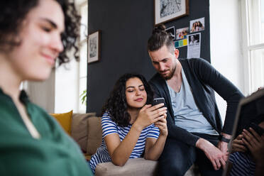 Eine Gruppe junger, fröhlicher Freunde mit Smartphone sitzt auf dem Sofa im Haus, Haus-Sharing-Konzept. - HPIF21959