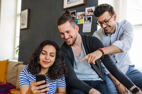 Eine Gruppe junger, fröhlicher Freunde mit Smartphone sitzt auf dem Sofa im Haus, Haus-Sharing-Konzept. - HPIF21961