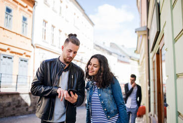 Young happy friends with a smartphone standing outdoor in town, talking. - HPIF21986