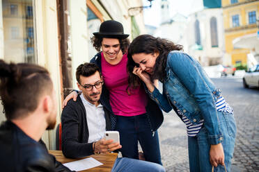 A group of young cheerful friends with smartphone sitting in an outdoor cafe, talking. - HPIF21990