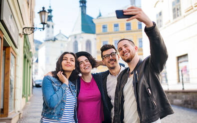 A group of young friends with smartphone standing outdoor in town, taking selfie. - HPIF21994