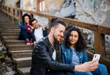 Freunde halten Erinnerungen mit ihren Smartphones fest, während sie auf der Stadttreppe sitzen und ein Gruppen-Selfie machen - HPIF22005