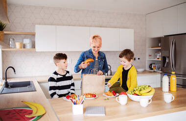 Eine glückliche junge Frau mit zwei Kindern beim Auspacken von Einkäufen in einer Küche. - HPIF22017