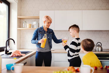 Eine junge Frau mit zwei glücklichen Kindern, die in einer Küche Orangensaft trinken. - HPIF22024