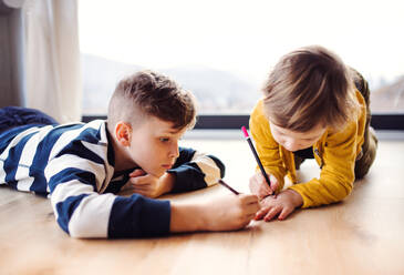 Portrait of two happy children lying on floor indoors at home, drawing. - HPIF22027