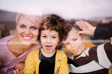 Porträt einer jungen Frau mit zwei Kindern zu Hause, die in die Kamera schaut, aufgenommen durch ein Glas. - HPIF22038