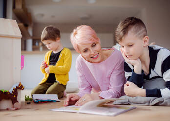 Eine junge Frau mit zwei Kindern, die ein Buch lesen und auf dem Boden spielen. - HPIF22040