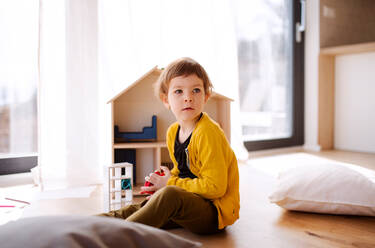 A small girl playing with a wooden house on the floor at home. - HPIF22049