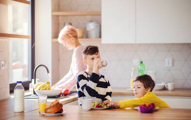 A young woman with two happy children eating fruit in a kitchen. - HPIF22054