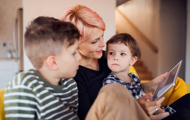 Eine junge Frau mit zwei Kindern sitzt zu Hause auf dem Sofa und benutzt ein Tablet. - HPIF22064