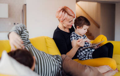 Eine junge Frau mit zwei Kindern sitzt zu Hause auf dem Sofa und benutzt ein Tablet. - HPIF22065