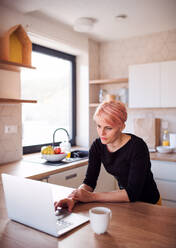 A young woman using laptop in a kitchen at home, working. - HPIF22074