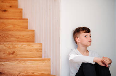 A small boy sitting on the floor by the stairs, grimacing. Copy space. - HPIF22083