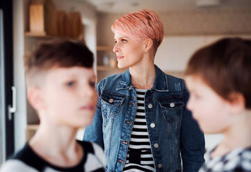 A young woman with two children standing at home, focus on background. - HPIF22098