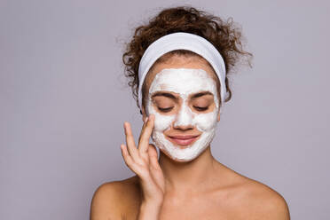 Porträt einer jungen Frau mit weißem Stirnband und Gesichtsmaske in einem Studio, Schönheit und Hautpflege. - HPIF22109