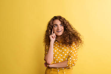 Porträt einer jungen glücklichen Frau in einem Studio auf gelbem Hintergrund, die nach oben schaut. - HPIF22119