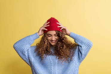 Porträt einer jungen Frau mit Wollmütze und Pullover in einem Atelier auf gelbem Hintergrund. - HPIF22120