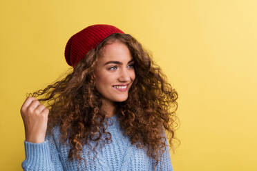 Portrait of a young woman with woolen hat and sweater in a studio on a yellow background. - HPIF22121