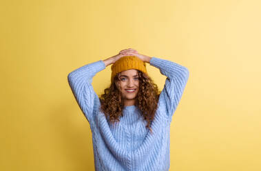 Porträt einer jungen Frau mit Wollmütze und Pullover in einem Atelier auf gelbem Hintergrund. - HPIF22122