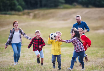 Eine Gruppe kleiner Schulkinder mit Lehrer auf einem Ausflug in die Natur, die mit einem Ball spielen. - HPIF22178