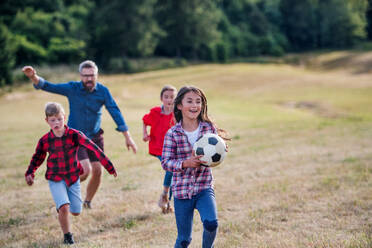 Eine Gruppe kleiner Schulkinder mit Lehrer auf einem Ausflug in die Natur, die mit einem Ball spielen. - HPIF22180