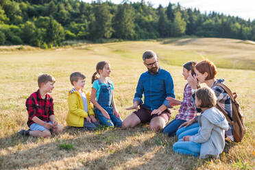 Gruppe von Schulkindern mit Lehrer auf Exkursion in der Natur, sitzend und redend. - HPIF22187