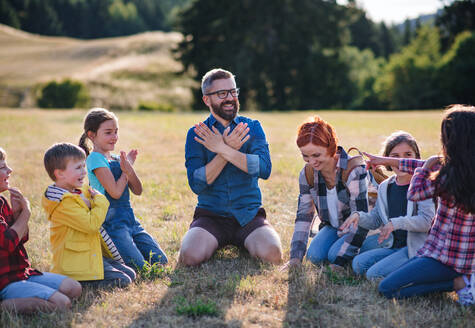 Eine Gruppe von kleinen Schulkindern mit einem Lehrer auf einem Ausflug in die Natur, die singen. - HPIF22189