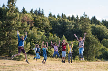 Eine Gruppe von kleinen Schulkindern mit Lehrer auf Exkursion in der Natur, springend. - HPIF22192