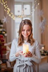 Porträt einer jungen Teenagerin, die zu Weihnachten zu Hause ist und eine Kerze hält. - HPIF22219