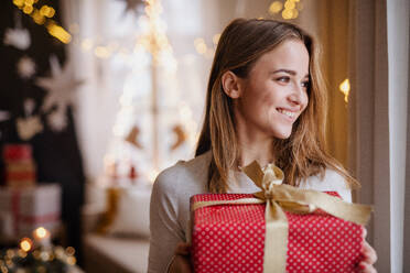 Porträt einer glücklichen jungen Frau, die zu Hause ein Weihnachtsgeschenk in der Hand hält. - HPIF22221