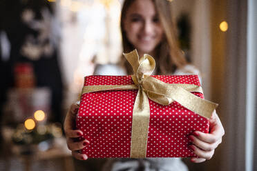 Porträt einer glücklichen jungen Frau, die zu Hause ein Weihnachtsgeschenk in der Hand hält. - HPIF22223