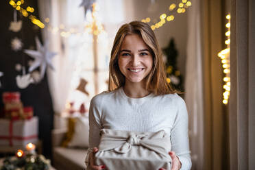 Porträt einer glücklichen jungen Frau, die zu Hause ein Weihnachtsgeschenk in der Hand hält. - HPIF22224