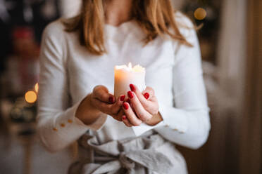 Unerkennbare junge Teenagerin zu Hause an Weihnachten, mit einer Kerze in der Hand. - HPIF22226