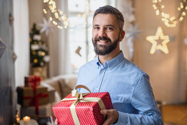 Porträt eines reifen Mannes, der zu Hause ein Weihnachtsgeschenk in der Hand hält. - HPIF22228