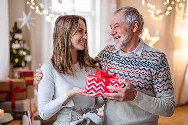 Glücklicher älterer Mann mit junger Frau zu Hause an Weihnachten, mit Geschenk in der Hand. - HPIF22234